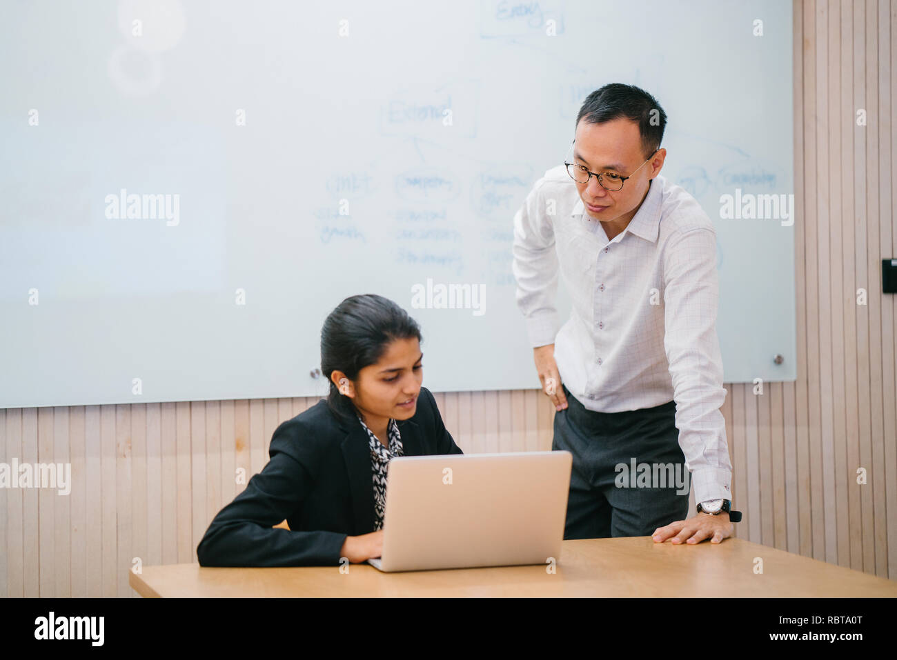 Un composite ont une réunion débat autour d'un ordinateur portable dans le bureau. Un homme d'origine chinoise et indienne parler intensément avec l'autre. Banque D'Images