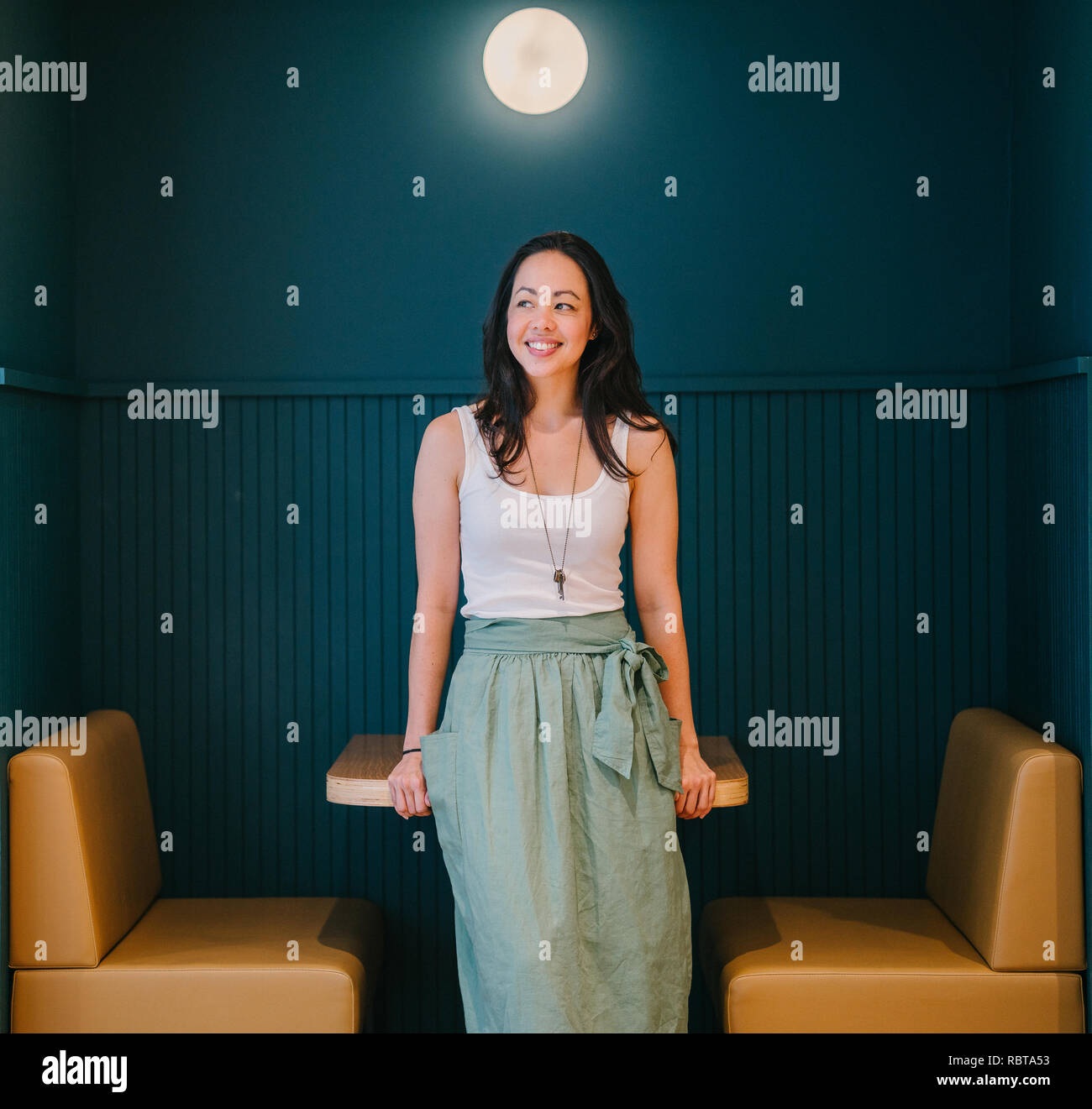 Portrait d'une jeune et belle asiatique femme assis sur une table d'un stand décoré avec goût dans son espace de coworking. Elle travaille dans une startup. Banque D'Images