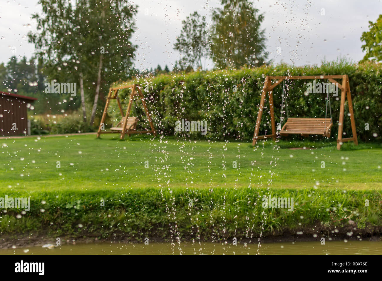 Deux bancs balançoire en bois dans le jardin avec des gouttes d'eau au premier plan. Fontaine eau gouttes dans l'air avec des balançoires de jardin à l'arrière-plan Banque D'Images