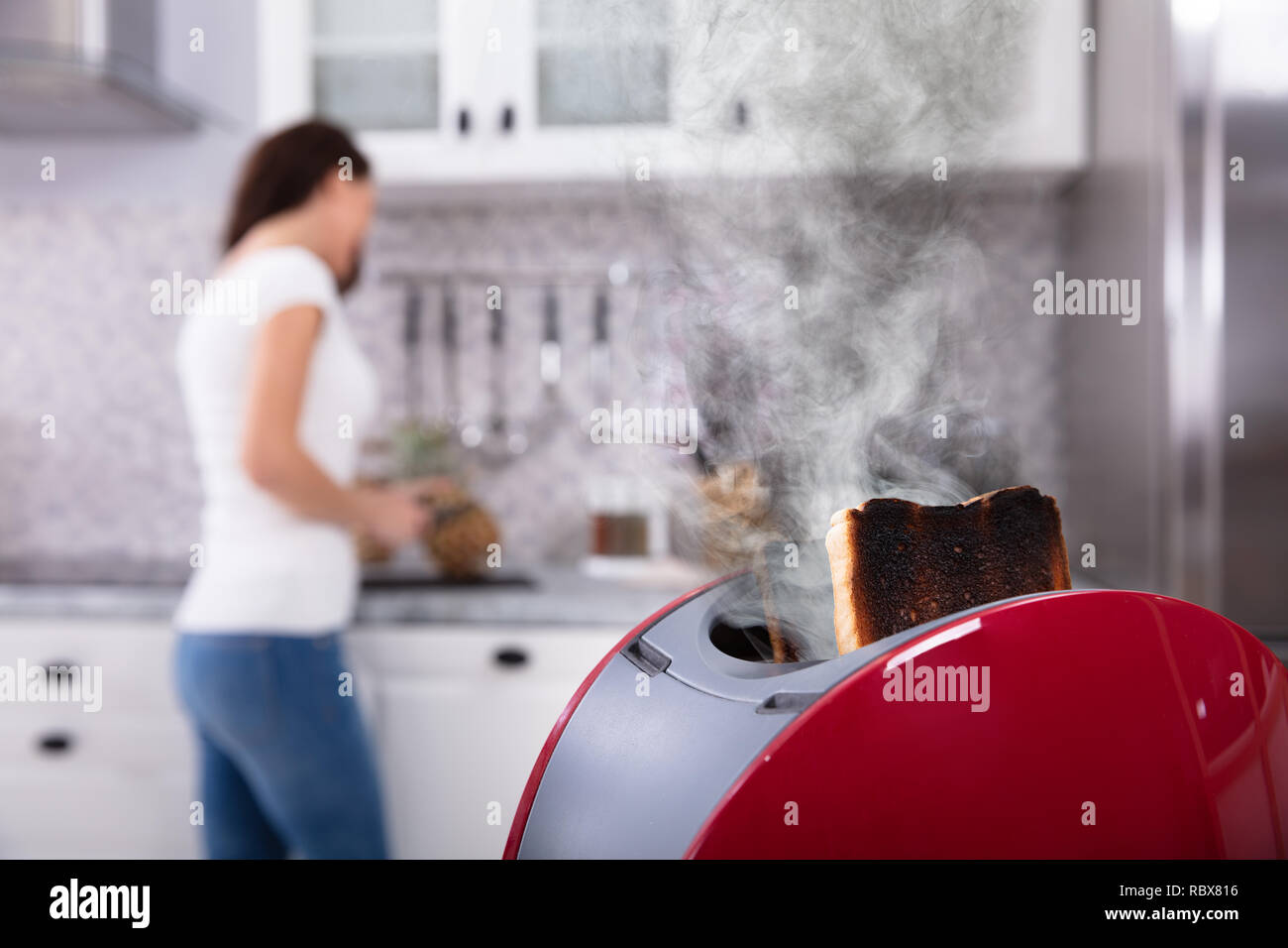 Close-up d'un grille-pain rouge avec Burnt Toast alors que Woman Working in Kitchen Banque D'Images