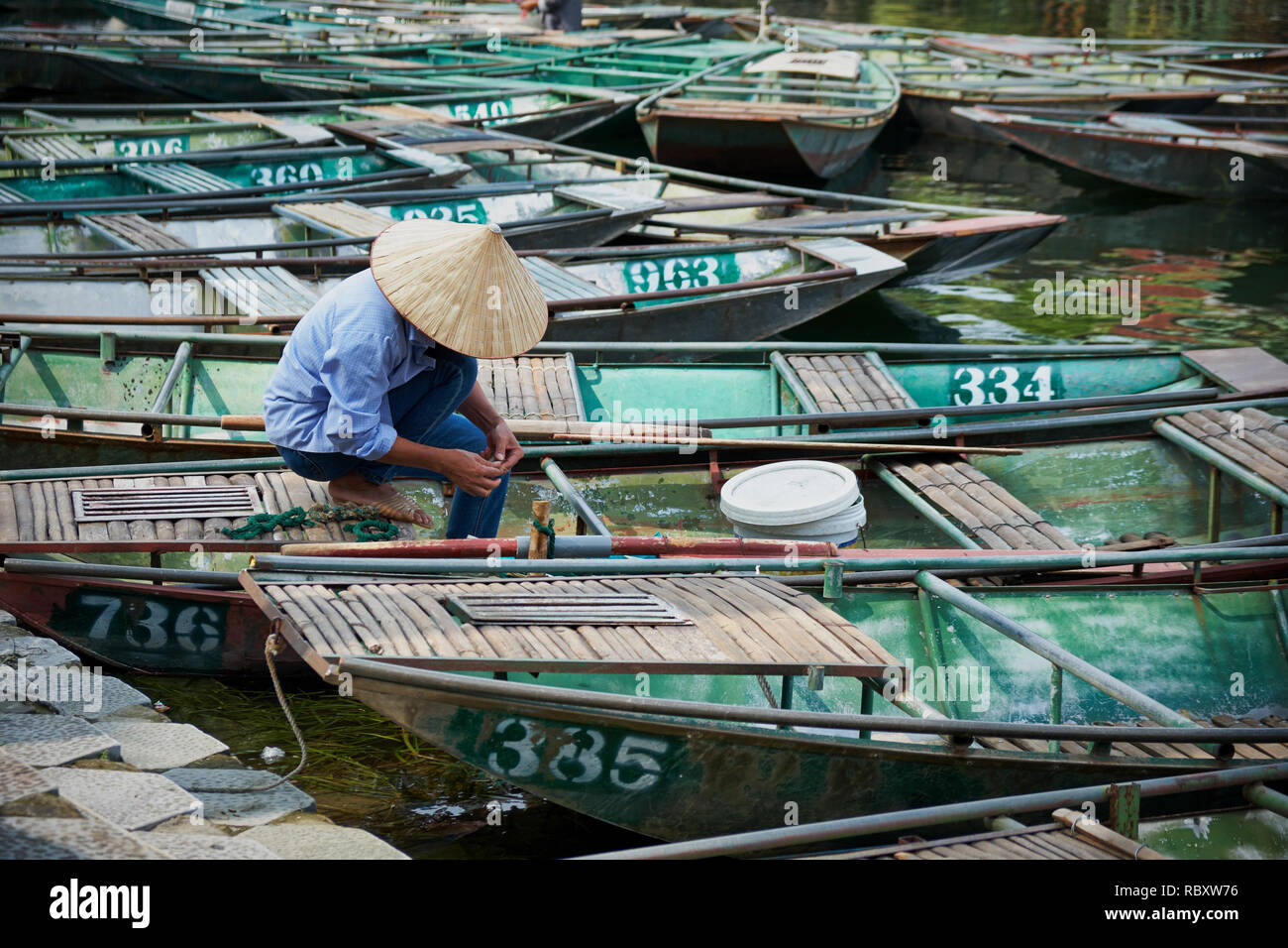 Man with hat vietnamiens travaillant dans un bateau, dans le port de Tam Coc, à Ninh Binh, Vietnam Banque D'Images
