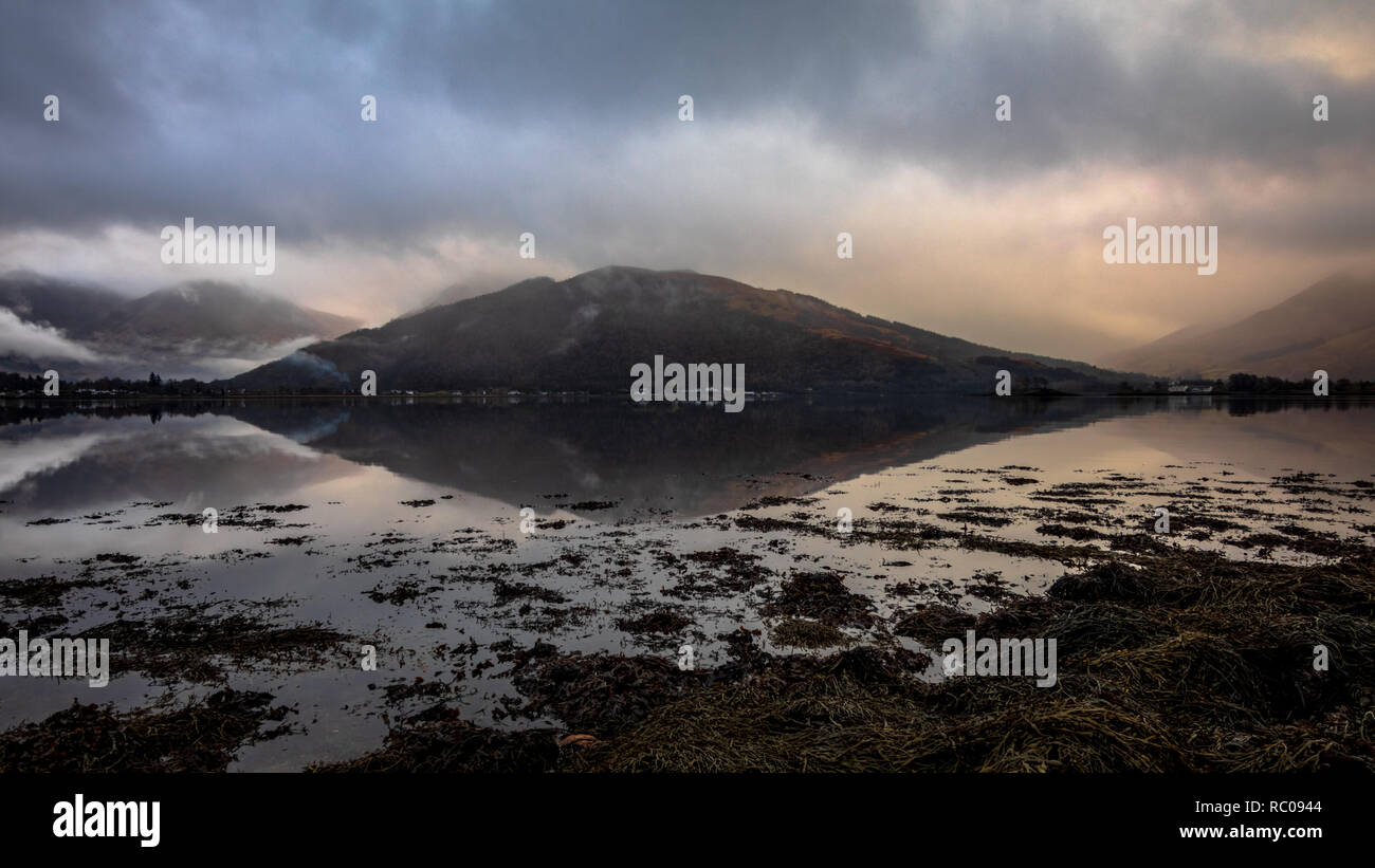 Tôt le matin dans le Loch Leven lac près de Kinlochleven au nord du nord de l'Écosse. Ciel nuageux avec un peu de soleil orange lights et réflexions fort comme un mirrow. Banque D'Images