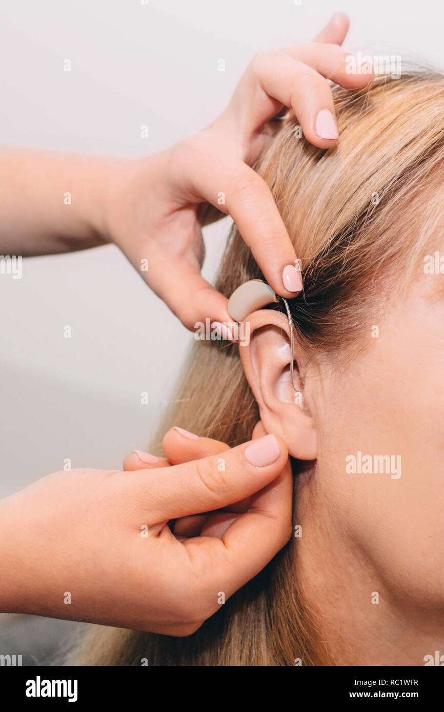 La main coupée de médecin l'ajustement d'aides auditives de l'oreille sur les femmes Banque D'Images