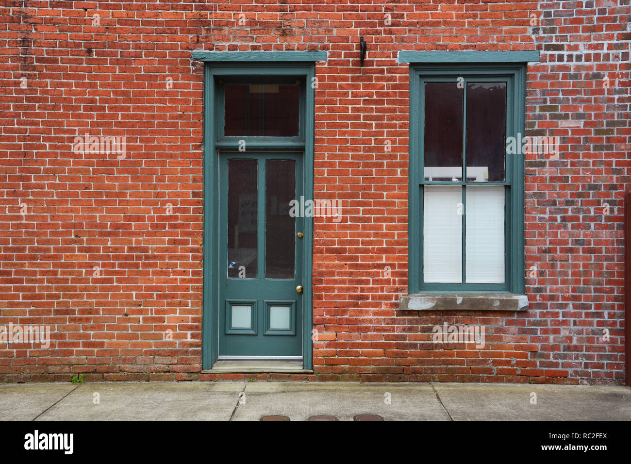 Une vieille porte et fenêtre en bois peint en vert contre un mur de brique rouge dans la petite ville de Elizabeth City, Caroline du Nord. Banque D'Images