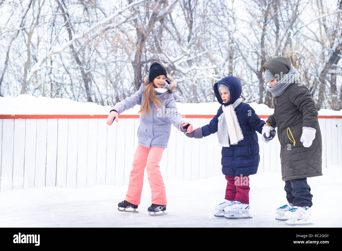 Les enfants tenant la main et profiter de l'apprentissage du patin à glace sur une patinoire dans un parc de neige pendant les vacances d'hiver Banque D'Images