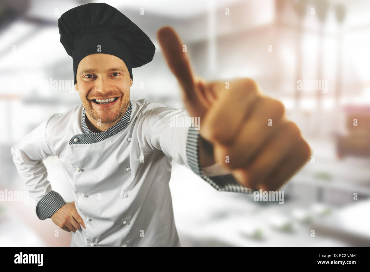 Young happy chef avec le pouce jusqu'à une cuisine de restaurant Banque D'Images