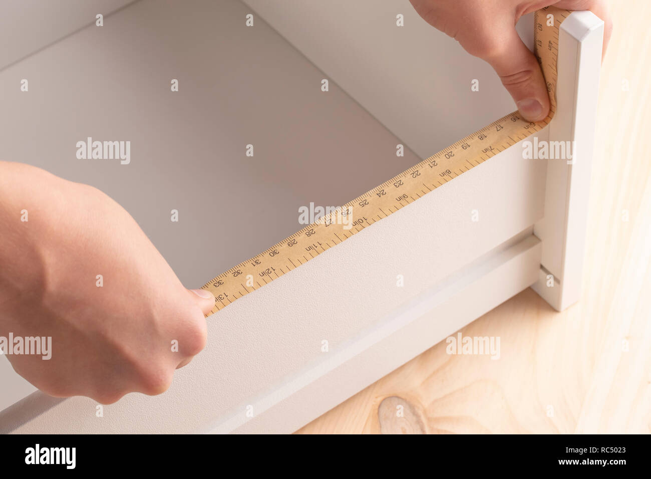 Un jeune homme tente de plier une table de chevet. Il mesure les étagères avec un outil de mesure. Banque D'Images