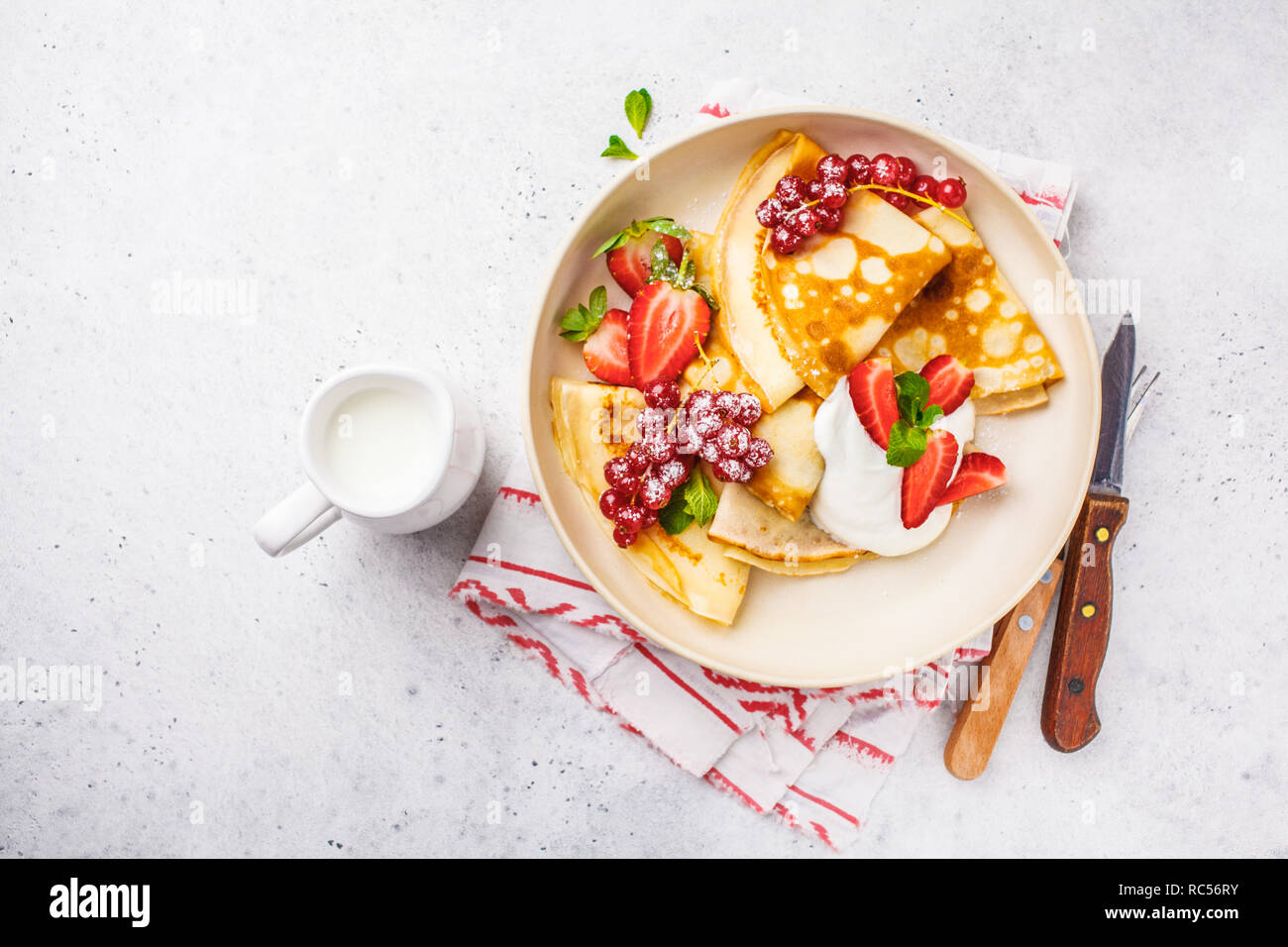 Des crêpes fines crème caillé, groseilles, fraises et du sucre en poudre en plaque blanche. Petit-déjeuner sain beau concept. Banque D'Images
