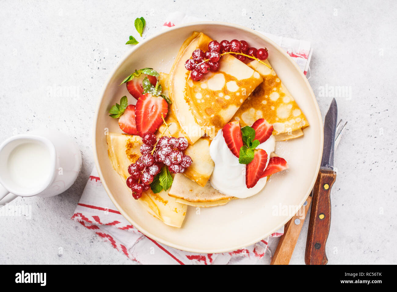 Des crêpes fines crème caillé, groseilles, fraises et du sucre en poudre en plaque blanche. Petit-déjeuner sain beau concept. Banque D'Images