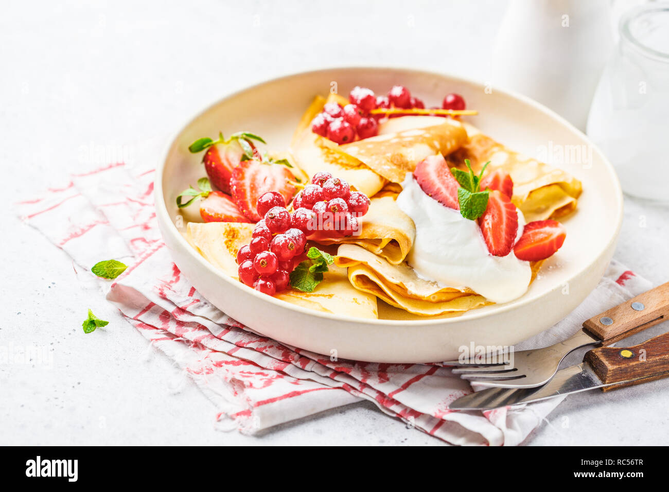 Des crêpes fines crème caillé, groseilles, fraises et du sucre en poudre en plaque blanche. Petit-déjeuner sain beau concept. Banque D'Images