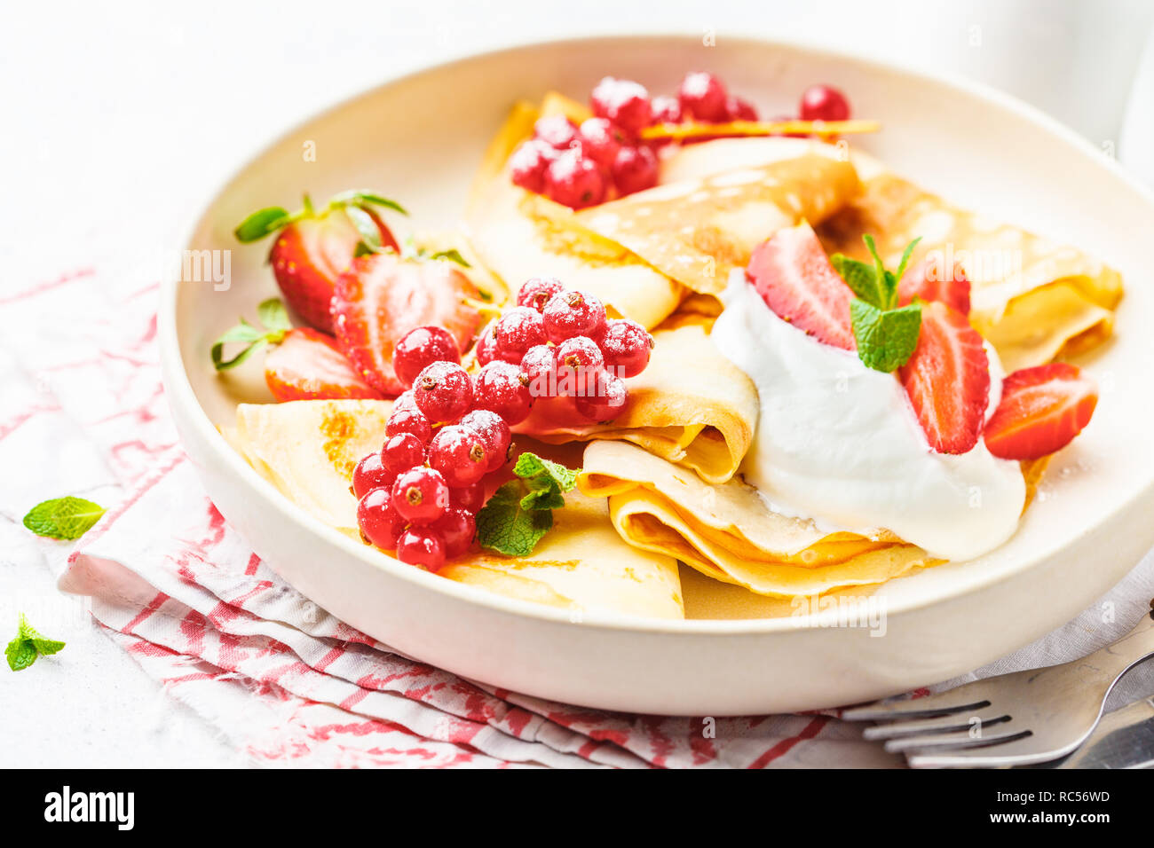 Des crêpes fines crème caillé, groseilles, fraises et du sucre en poudre en plaque blanche. Petit-déjeuner sain beau concept. Banque D'Images