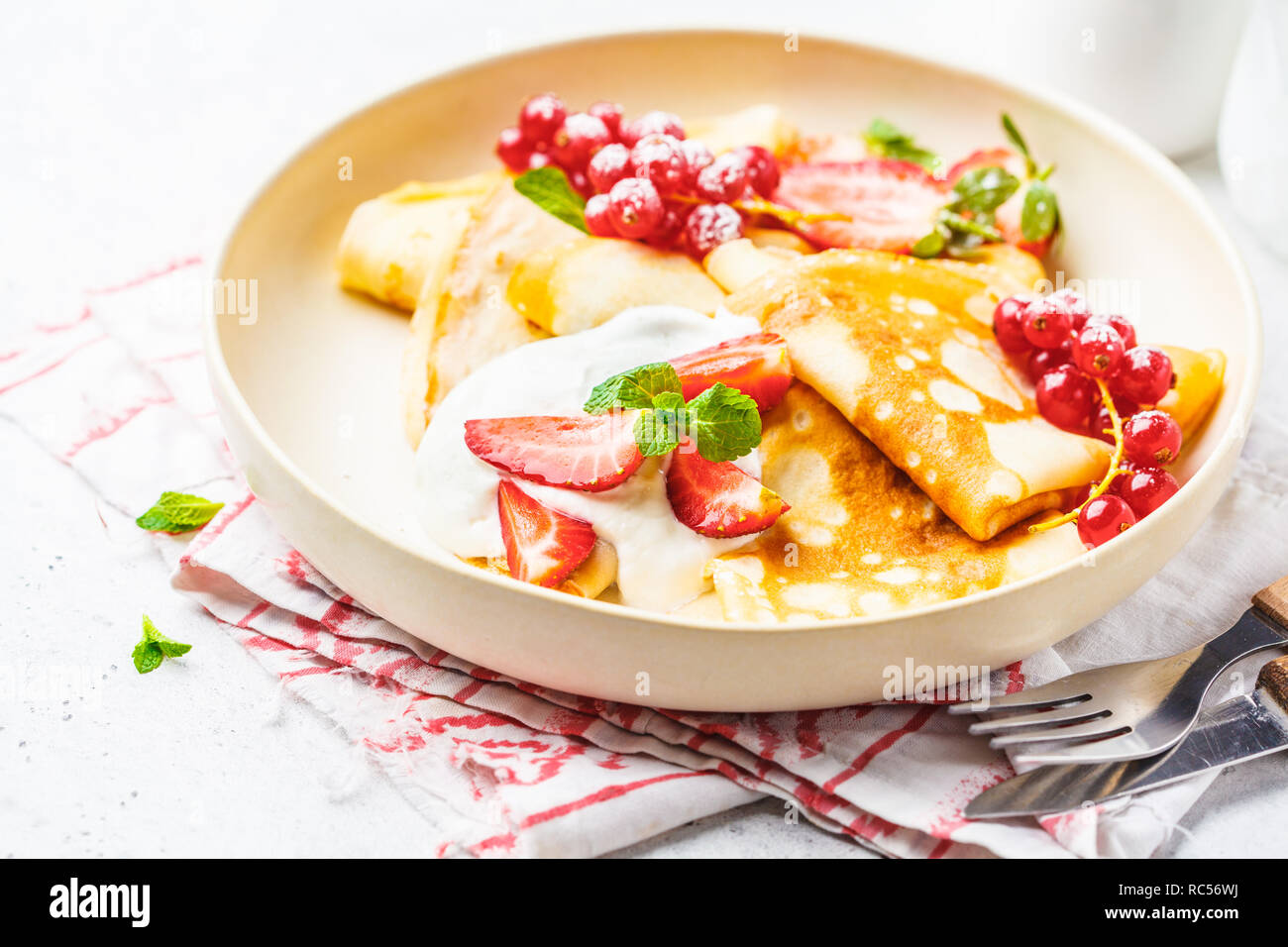 Des crêpes fines crème caillé, groseilles, fraises et du sucre en poudre en plaque blanche. Petit-déjeuner sain beau concept. Banque D'Images