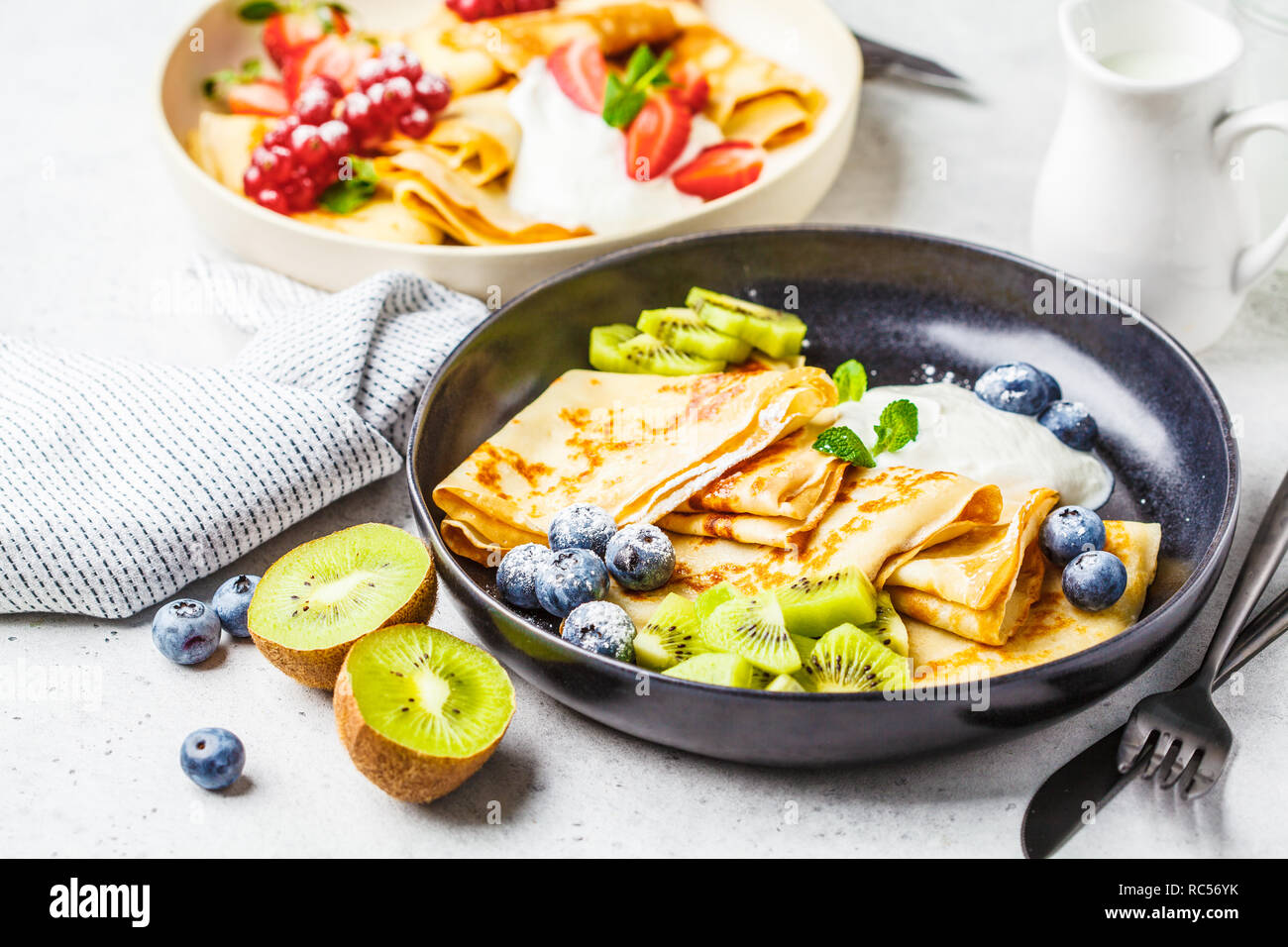 Crêpes minces faits maison servis avec crème de fromage, fruits et baies en noir et blanc des plaques. Petit-déjeuner sain beau concept. Banque D'Images