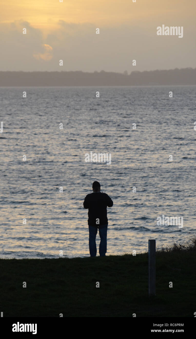 Silhouette d'une personne dans la lumière du soir, avec la mer en arrière-plan. Banque D'Images