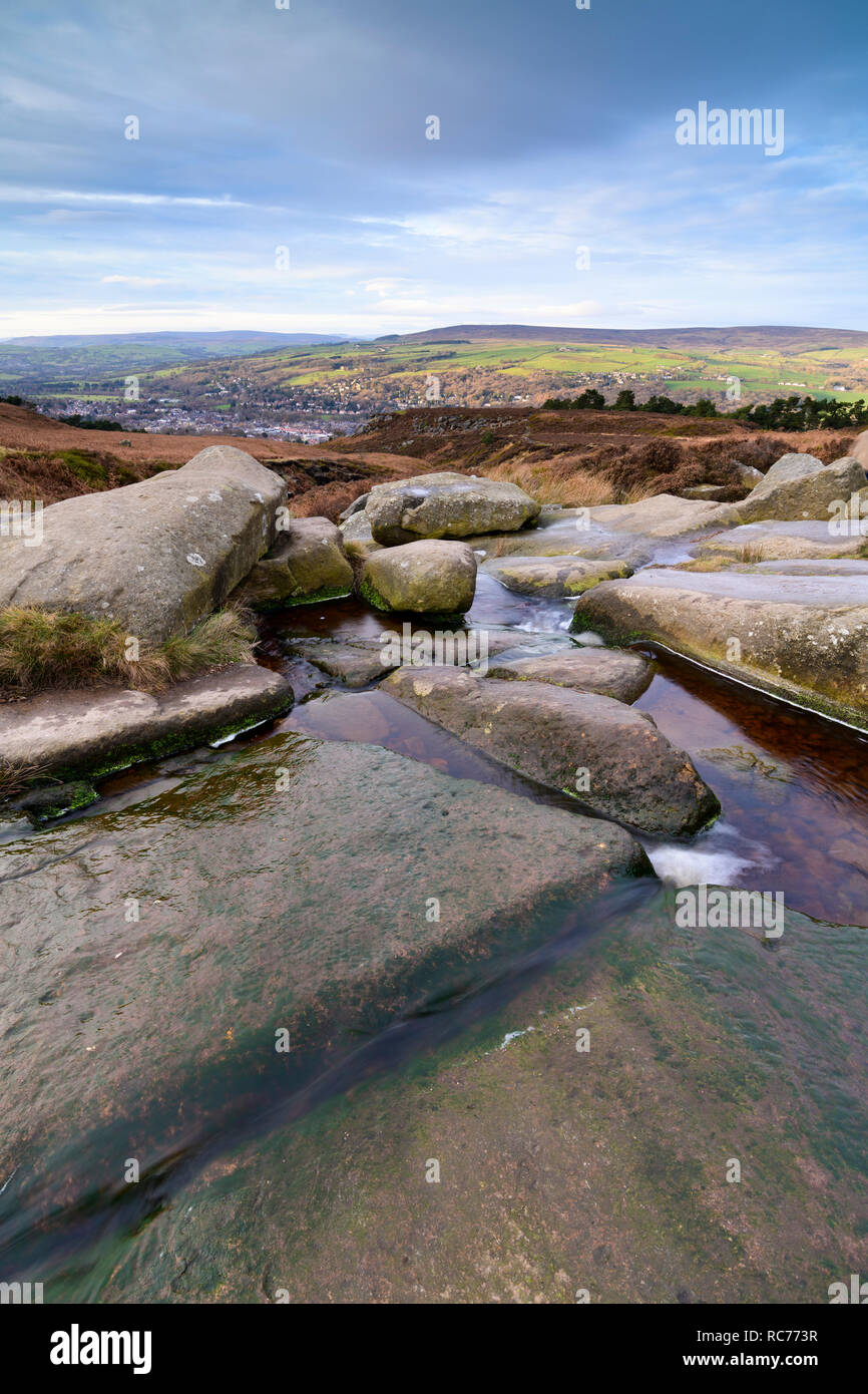 Rural pittoresque vue ensoleillée sur les collines et ville nichée dans la vallée, à partir de la Wharfe éperon rocheux & stream, en haut d'Ilkley Moor - West Yorkshire, Angleterre, Royaume-Uni. Banque D'Images