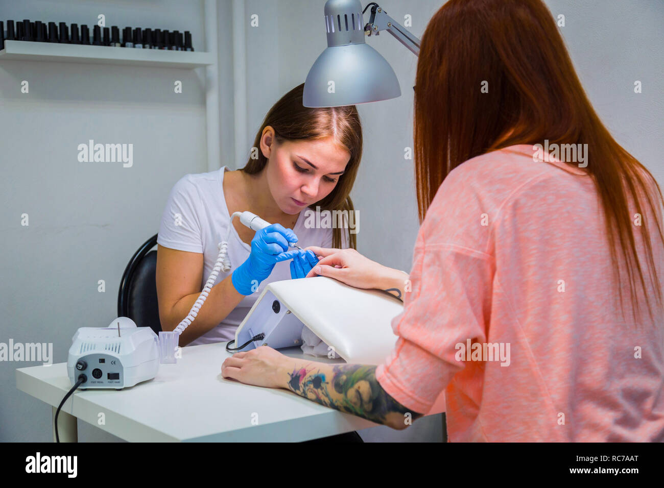 Femme dans un salon de manucure recevant une manucure par une esthéticienne avec lime à ongles électrique. Woman getting nail manucure. Limer les ongles coiffeur à un client Banque D'Images