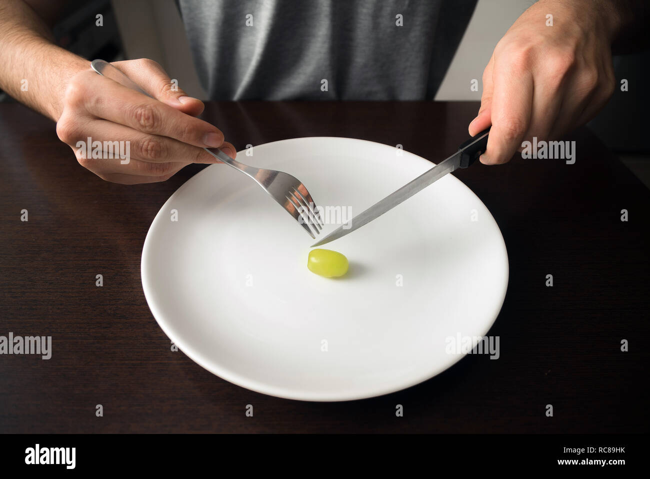 Thème : alimentation saine mains tenant le couteau et la fourchette sur une assiette avec du raisin vert sur une assiette blanche Banque D'Images