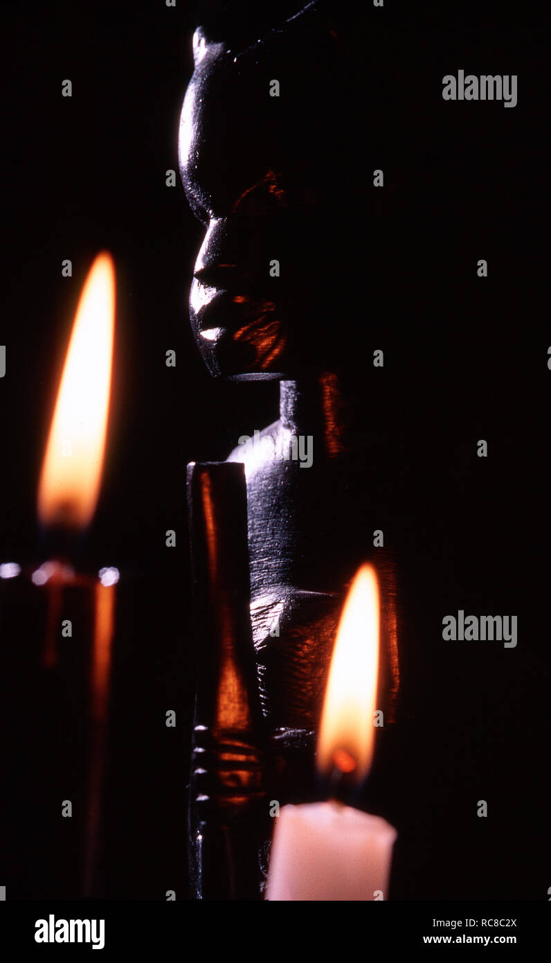 Dark image en gros plan d'une statuette africaine avec deux bougies brûlantes Banque D'Images