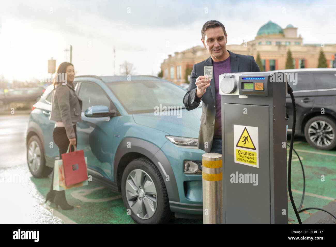 L'homme et la femme à la voiture électrique de charge charge voiture Park, Manchester, UK Banque D'Images
