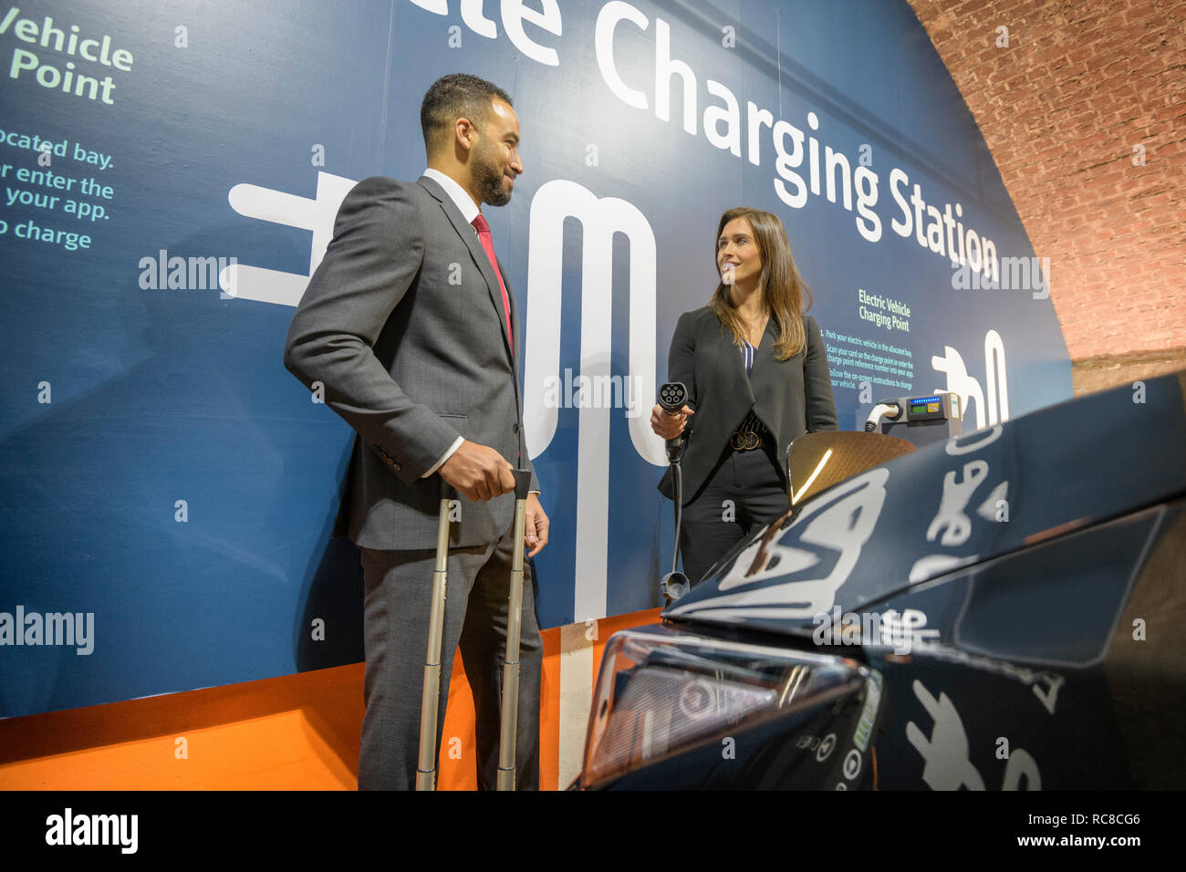 Businessman and businesswoman at station de charge de véhicules électriques, Manchester, UK Banque D'Images