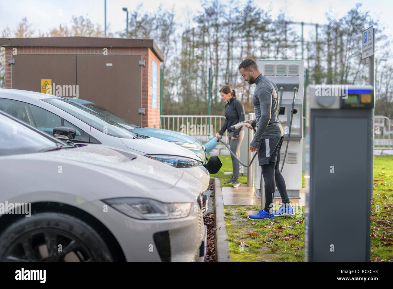 Sportsman et femme voiture électrique de charge à l'emplacement de chargement, Manchester, UK Banque D'Images