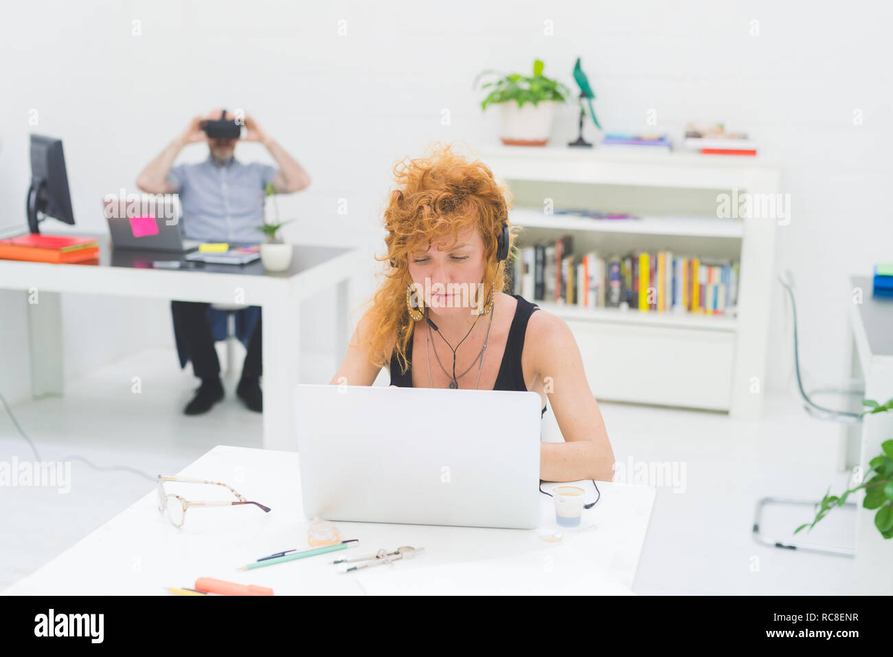 Businesswoman typing on laptop at office desk lors de l'écoute au casque Banque D'Images