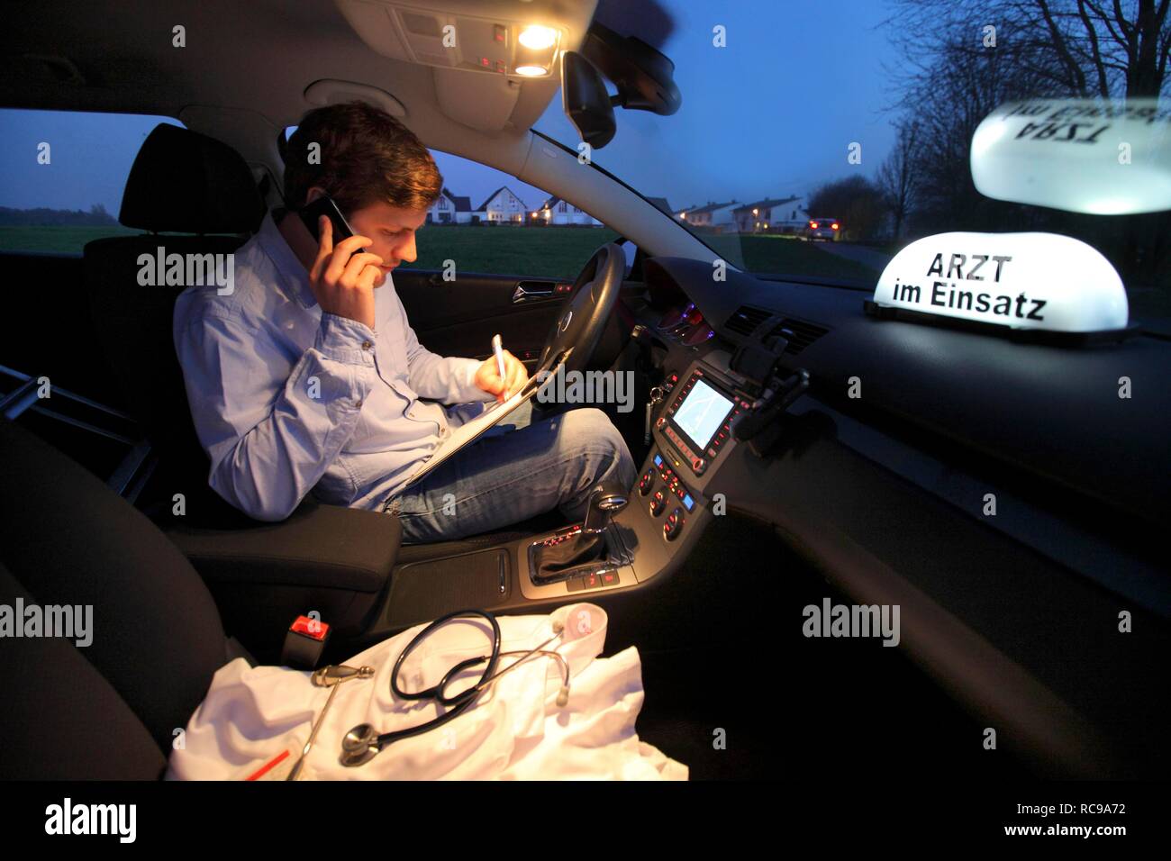 Jeune médecin, omnipraticien travaillant dans le pays, faisant appel téléphonique et prend des notes dans sa voiture après une soirée home Banque D'Images Jeune médecin, omnipraticien travaillant dans le pays, faisant appel téléphonique et prend des notes dans sa voiture après une soirée home Banque D'Images
