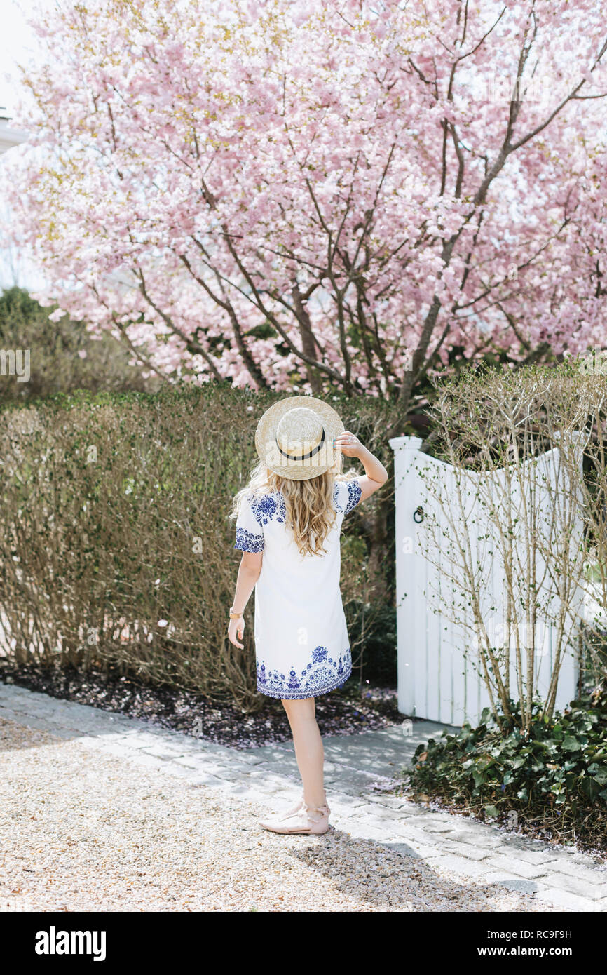 Jeune Femme au chapeau de paille en face de l'arbre rose blossom, vue arrière, Menemsha, Martha's Vineyard, Massachusetts, USA Banque D'Images