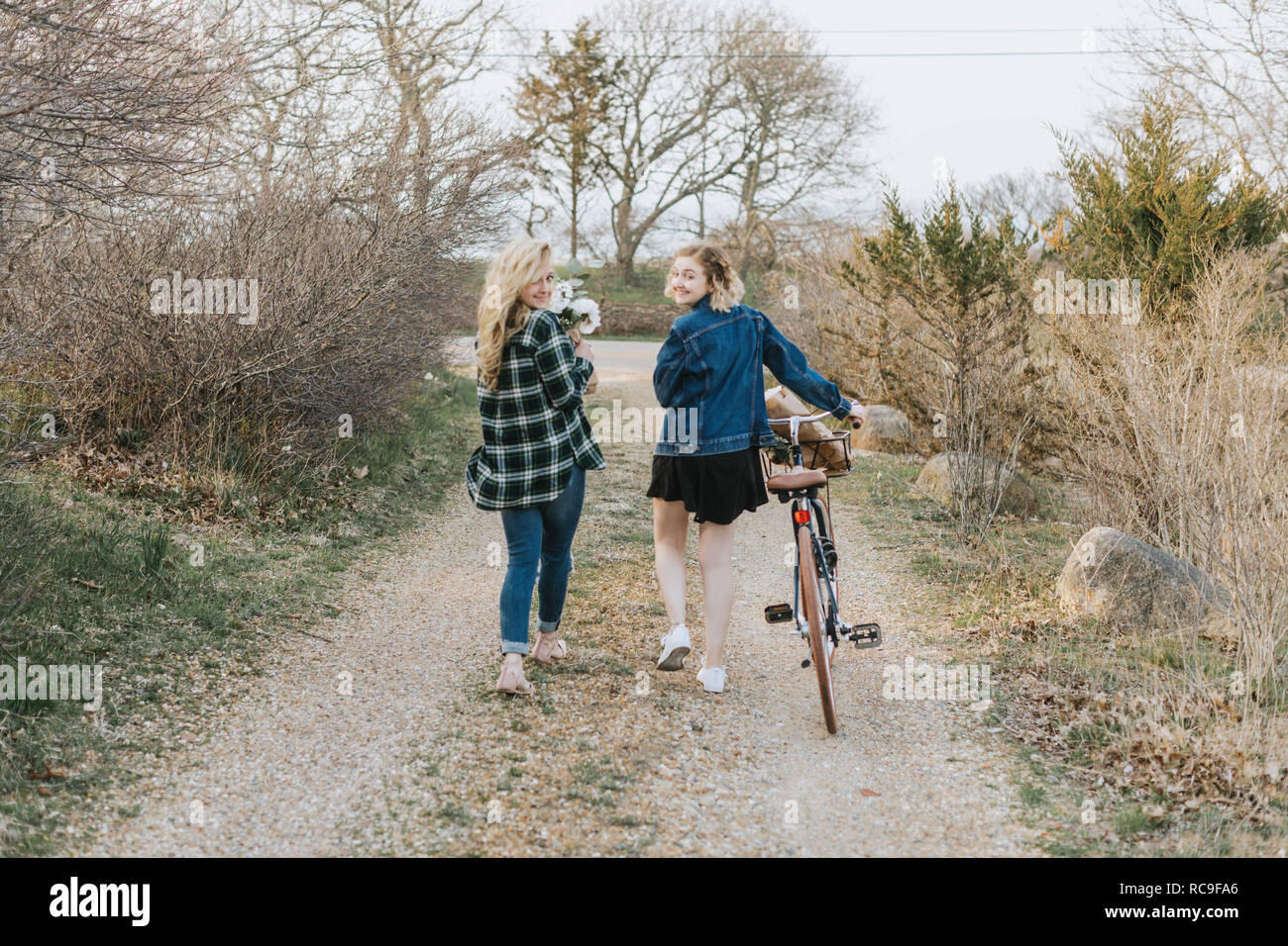 Deux jeunes femmes en poussant la bicyclette sur piste rurale, vue arrière portrait, Menemsha, Martha's Vineyard, Massachusetts, USA Banque D'Images
