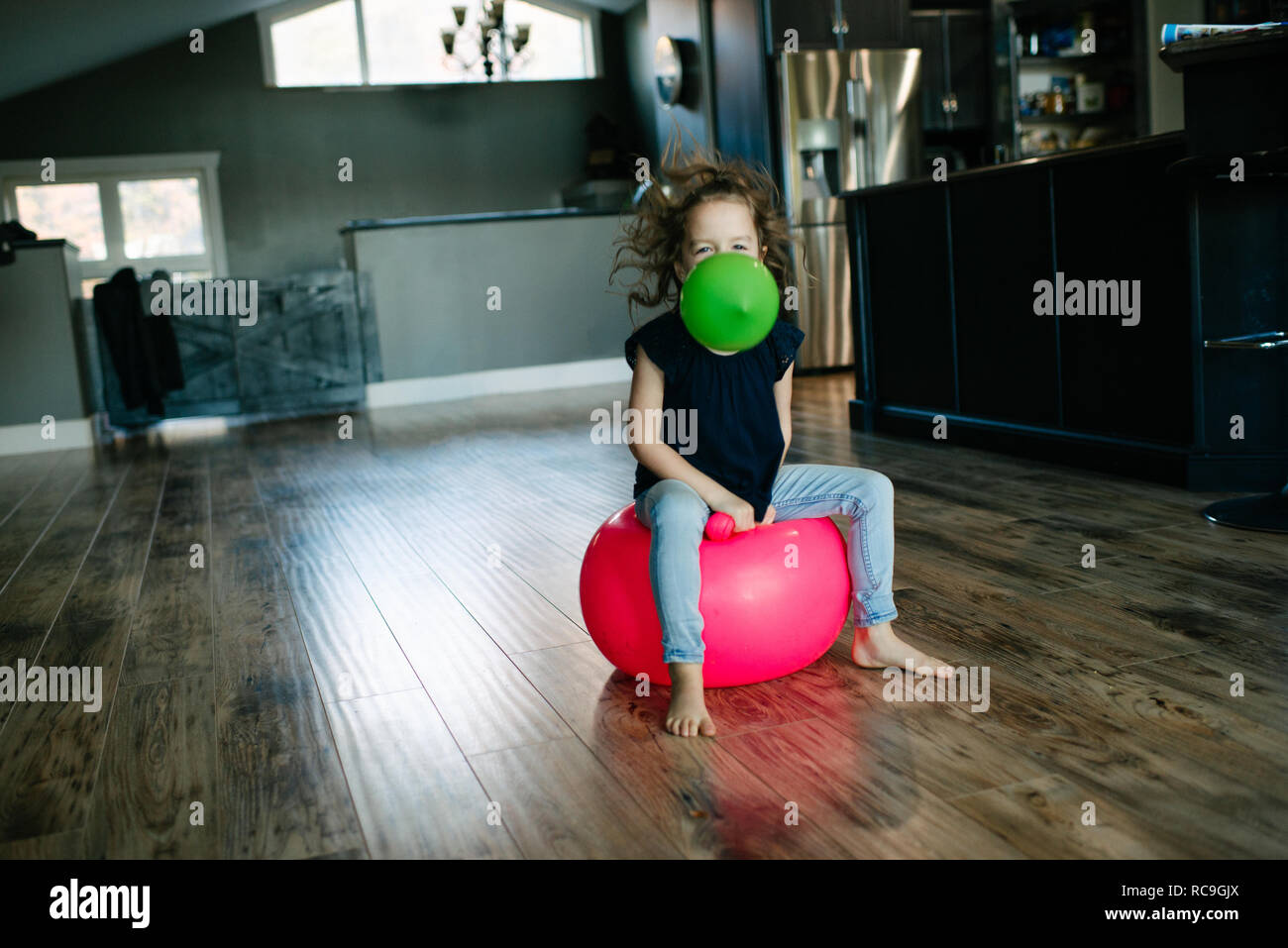 Petite fille avec ballon en bouche rebondissent sur ballon de gymnastique à la maison Banque D'Images