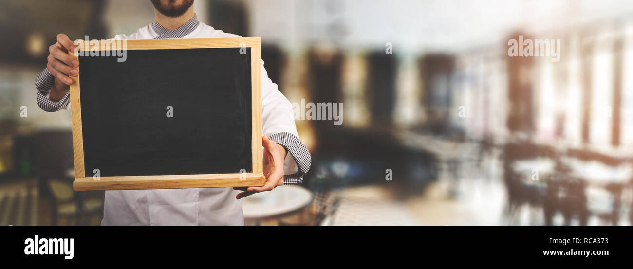 Chef avec tableau noir vierge debout dans un restaurant. banner copy space Banque D'Images