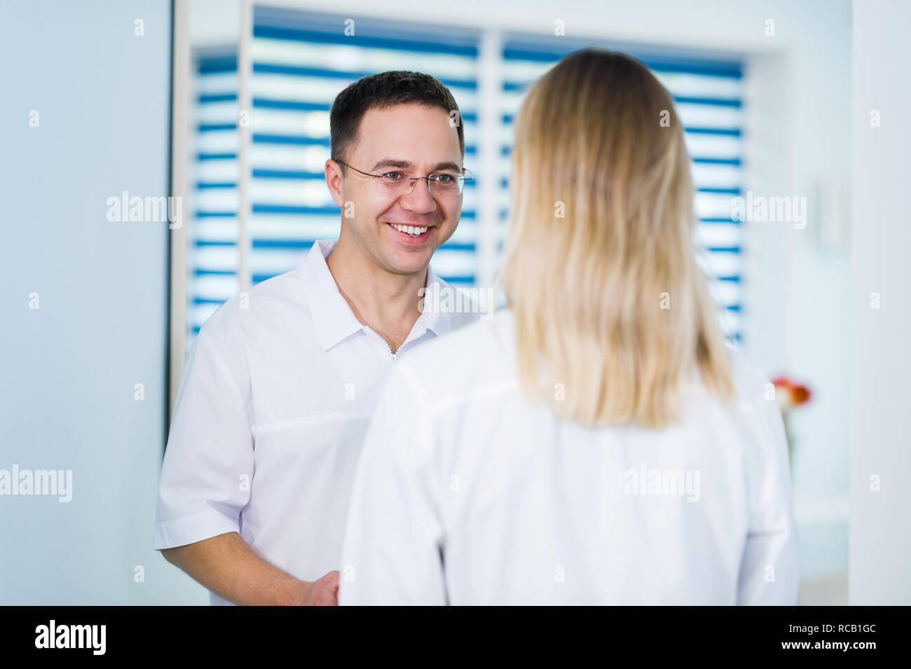 Beau jeune médecin parle avec sa belle assistante, debout dans salle d'attente du centre Banque D'Images