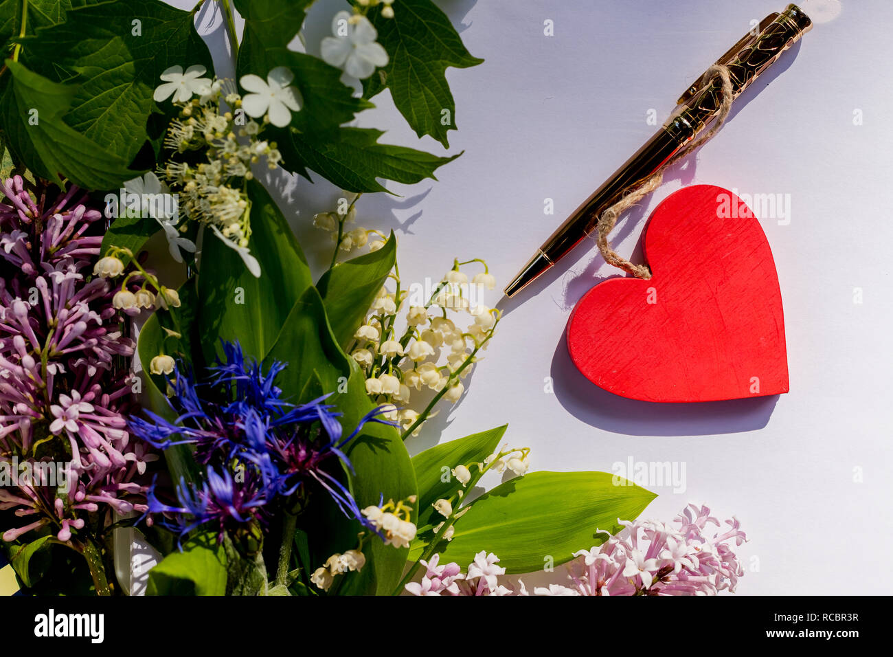 Maquette lettre avec un coeur en bois rouge,l'amour se trouve sur papier blanc vide avec des fleurs, lilas, muguet, barbeaux.carte de souhaits pour la Saint-Valentin. Mise à plat, haut voir photo.lettre d'amour concept Banque D'Images