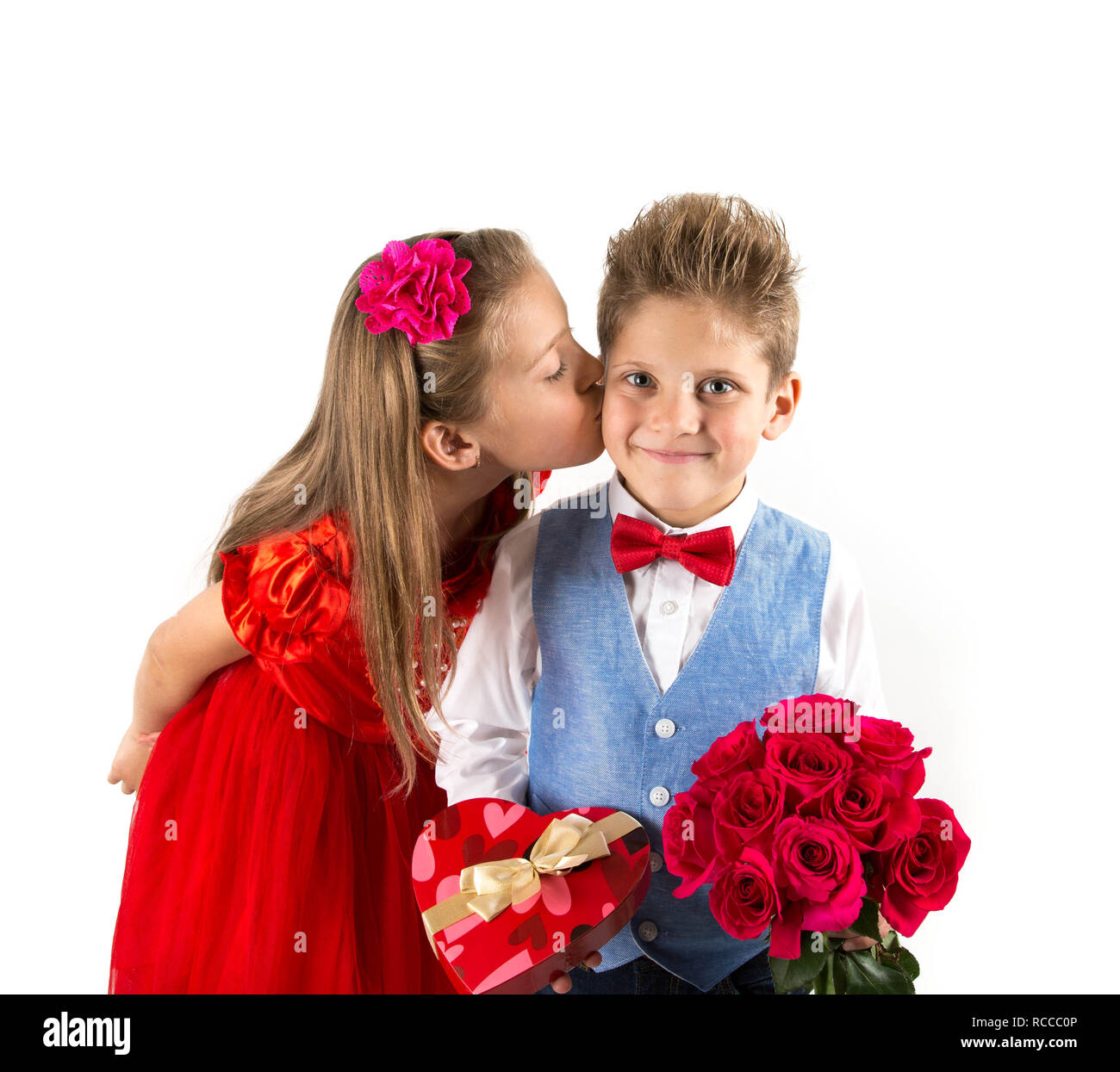 Saint Valentine's day. Jolie fille avec robe rouge embrasser un garçon gentleman avec gilet bleu, rouge cravate papillon, roses rouges en forme de coeur et godet b cadeaux Banque D'Images