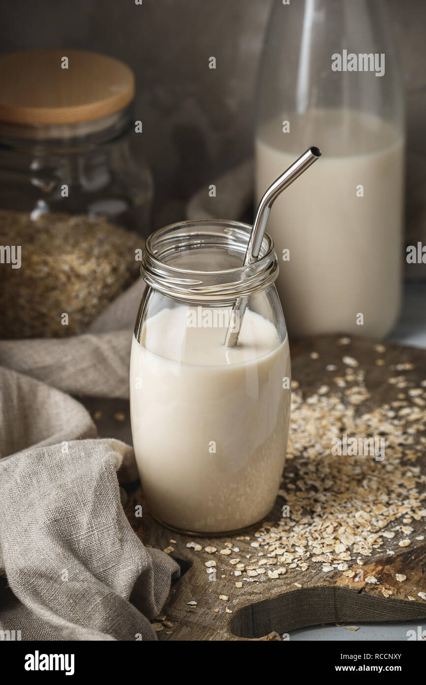 L'avoine non dairy lait dans un bocal en verre avec paille réutilisable métal sur fond rustique. Flocons d'avoine éparpillées sur la table. Banque D'Images