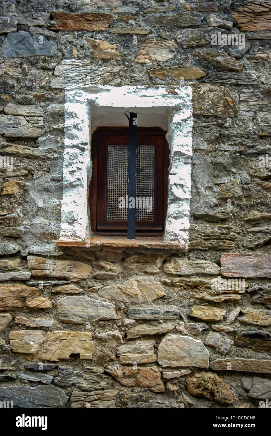 Très petite fenêtre découpée dans le mur de pierre d'une maison française, avec barre de sécurité et sur le châssis peint en blanc Banque D'Images