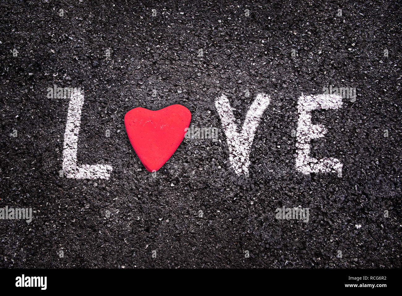 Carte de Saint Valentin, mot amour écrit sur fond d'asphalte avec une pierre rouge en forme de cœur Banque D'Images