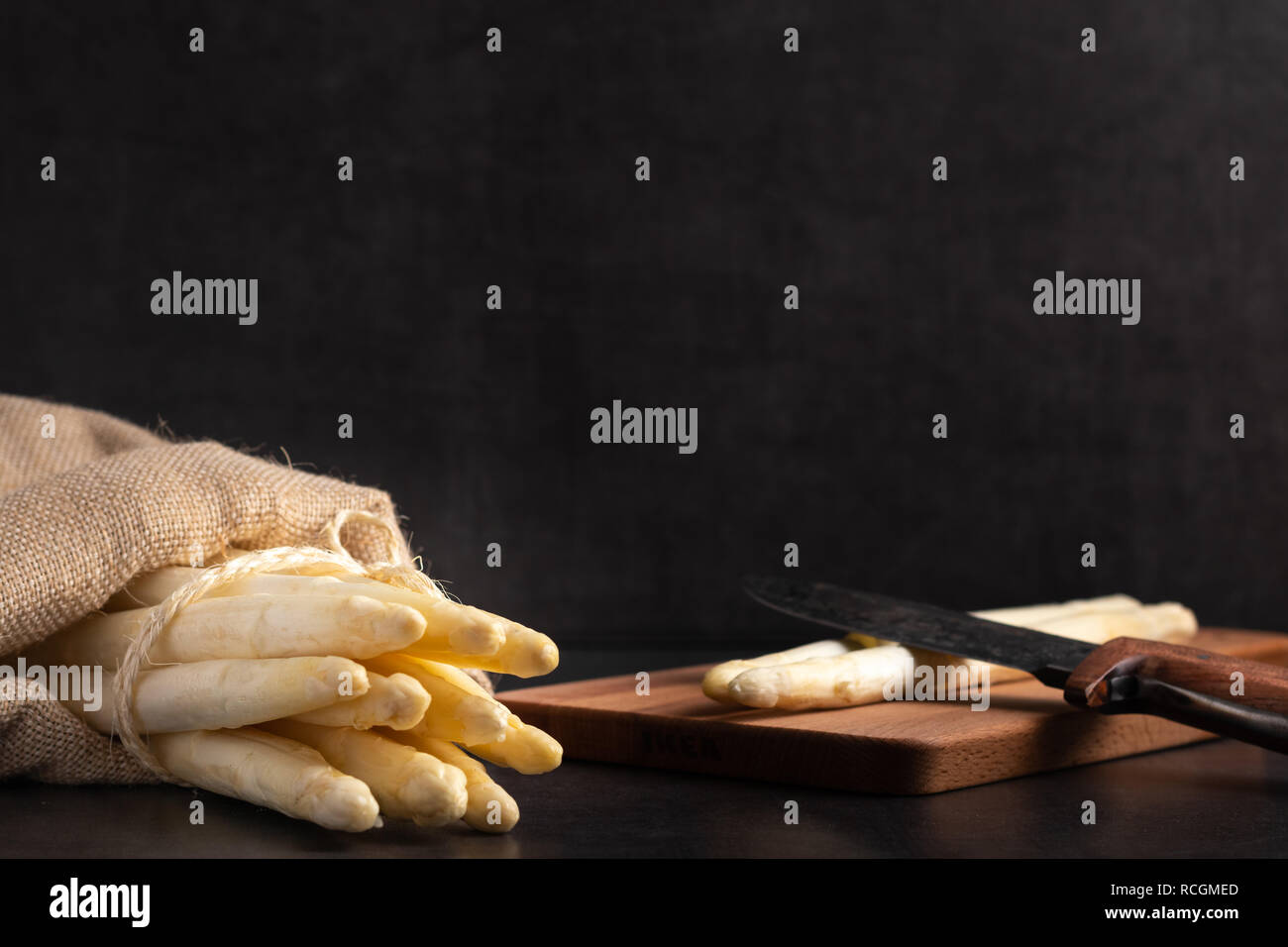 Asperges fraîchement récoltées dans un sac de jute sur une planche à découper en bois Banque D'Images