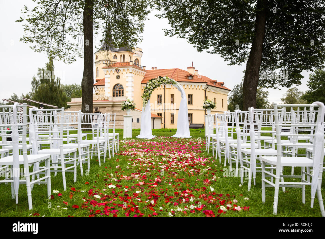 Décorées avec passage de mariage et les fleurs en tissu à l'extérieur. Cérémonie de mariage sur la pelouse verte, couverte de pétales de rose dans le contexte du château Banque D'Images