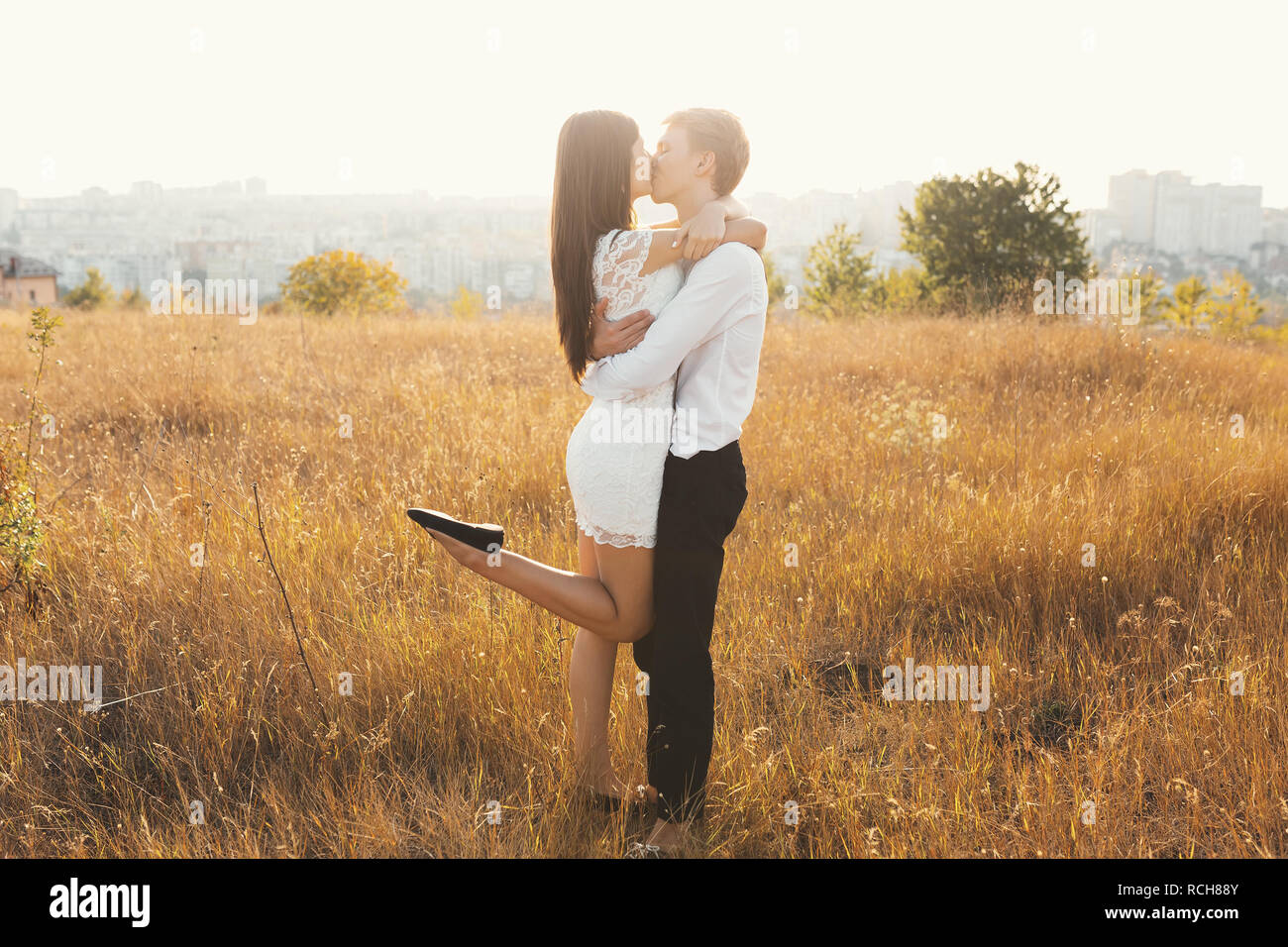 Couple aimant habillé en blanc à l'extérieur, s'embrasser, toucher doux les uns les autres avec un beau paysage en arrière-plan, l'herbe d'or - Concept de pe Banque D'Images