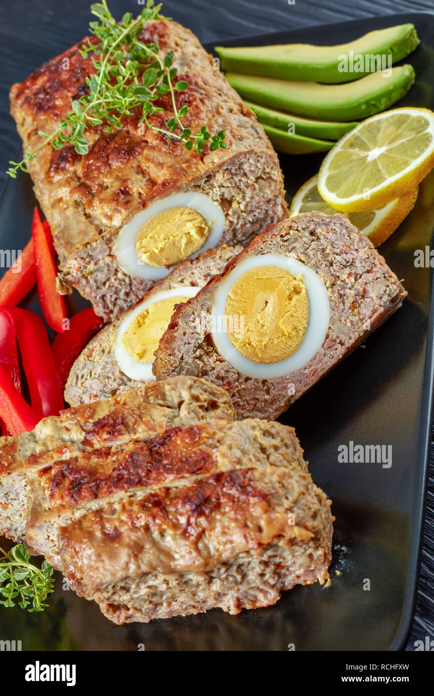 Viande farcies d'œufs servis avec red bell peppe, citron et de tranches d'avocat sur un plateau rectangulaire noir sur une table de bois, vue verticale d'en haut Banque D'Images