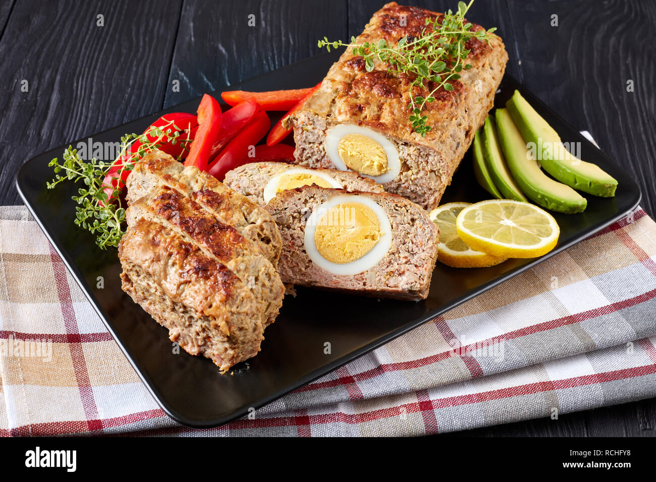 Viande Bolo de Carne Alemao servi avec des tranches d'avocat et de poivron rouge sur un plateau rectangulaire noir sur une table de bois, vue verticale d'en haut Banque D'Images