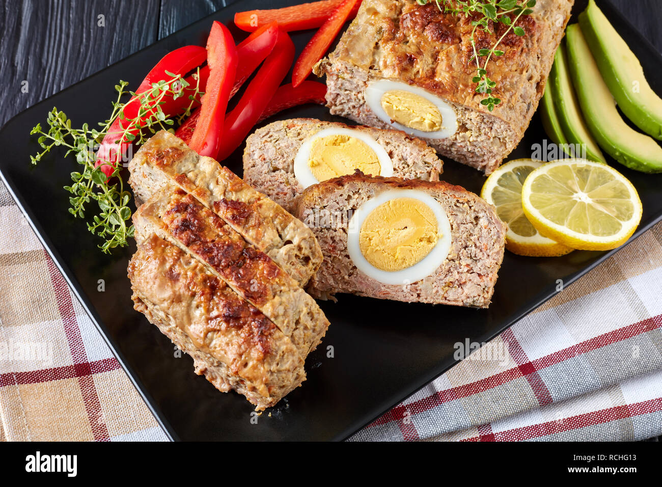 Vue de dessus de tranches de pain de viande servi avec des tranches d'avocat et de poivron rouge sur un plateau rectangulaire noir sur une table de bois, vue de dessus, close-up Banque D'Images