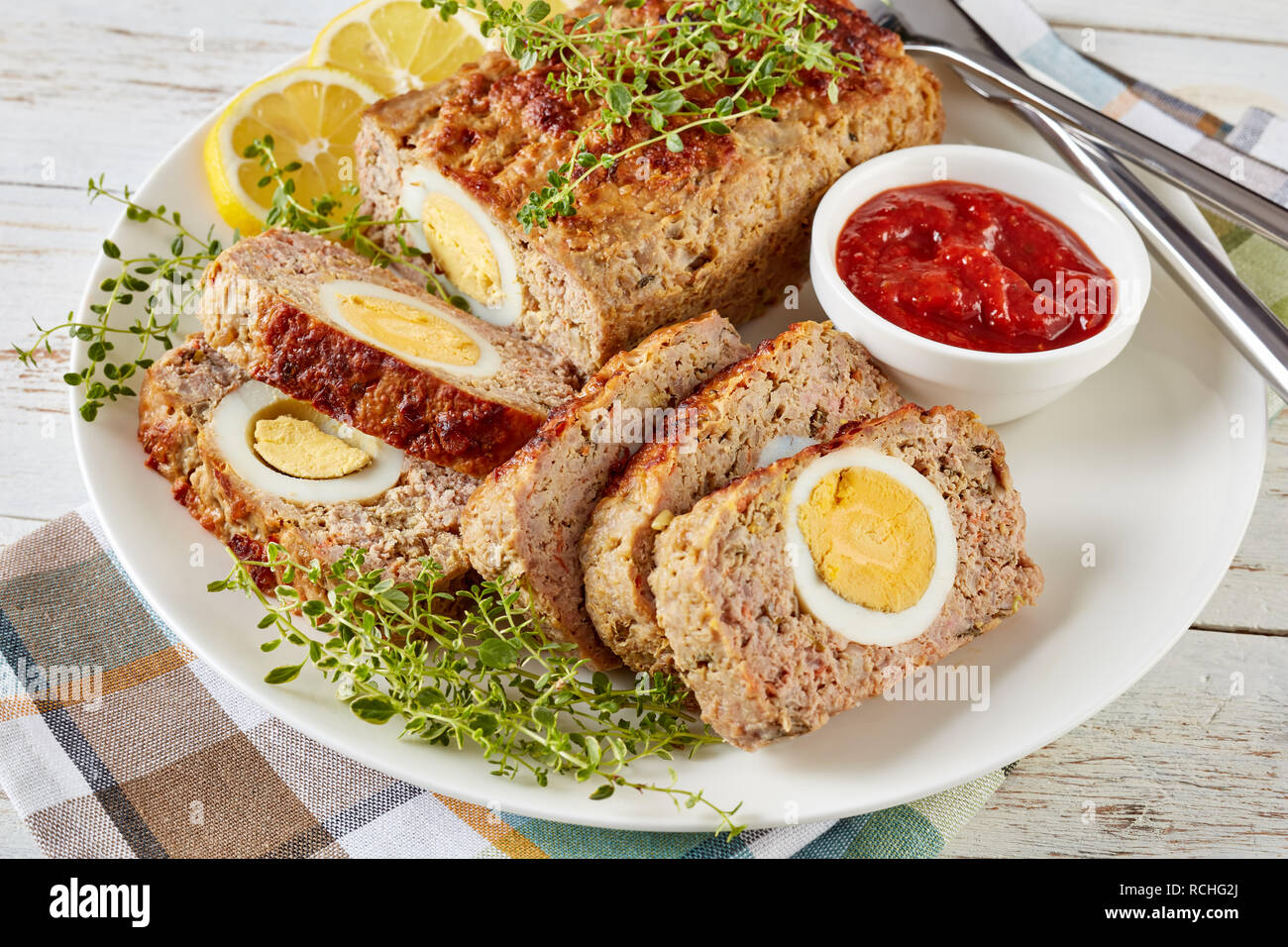 Viande farcies avec oeuf dur servi avec une sauce tomate et des rondelles de citron sur une plaque blanche sur une vieille table en bois, vue de dessus, close-up Banque D'Images