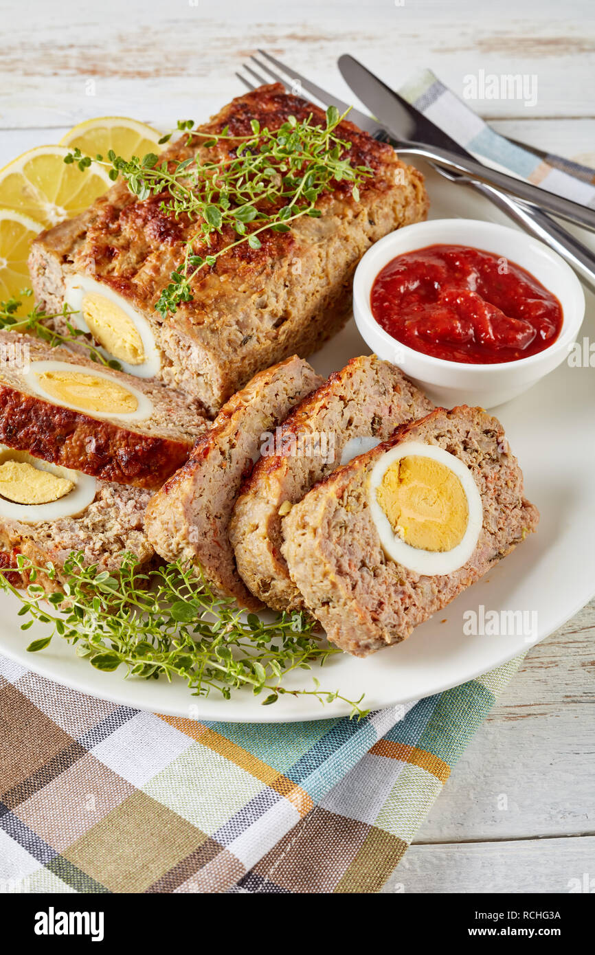 Tranches de viande farcies avec oeuf dur servi avec une sauce tomate et des rondelles de citron sur une plaque blanche sur une vieille table en bois, vue verticale de ab Banque D'Images