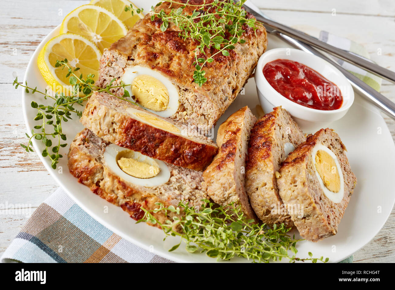 Tranches de viande farcies avec oeuf dur servi avec une sauce tomate et des rondelles de citron sur une plaque blanche avec fourchette et couteau sur une vieille table en bois, v Banque D'Images