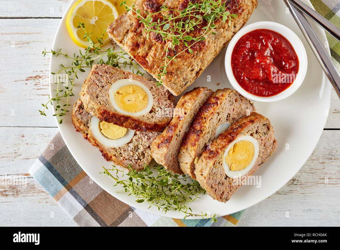 Tranches de viande farcies avec oeuf dur servi avec une sauce tomate et des rondelles de citron sur une plaque blanche avec fourchette et couteau sur une vieille table en bois, v Banque D'Images