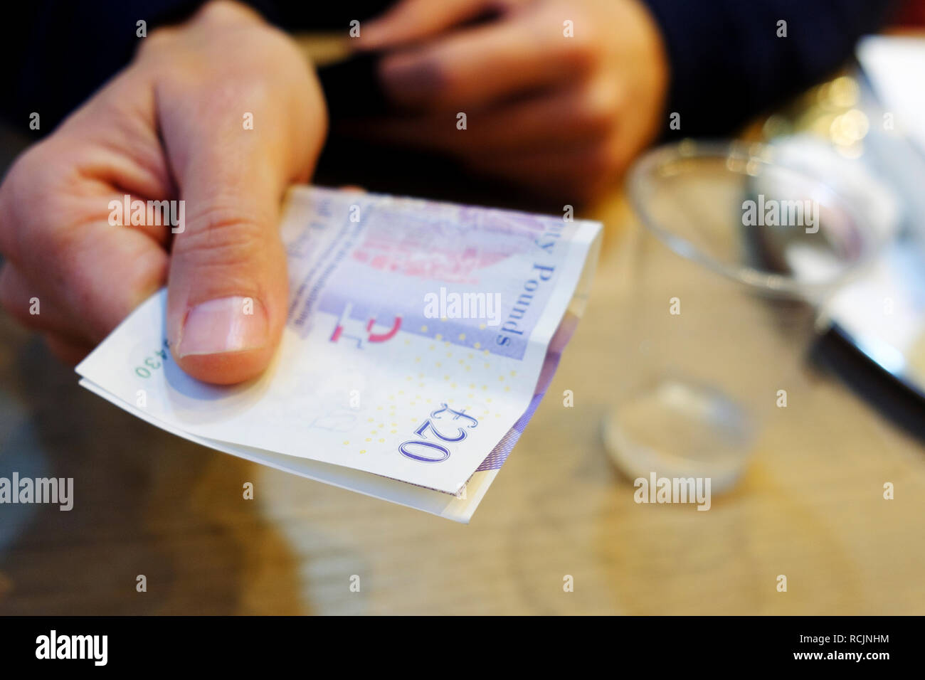 Libre d'un jeune homme de race blanche assise sur une table à propos de payer la facture avec un billet de 20 livres sterling Banque D'Images