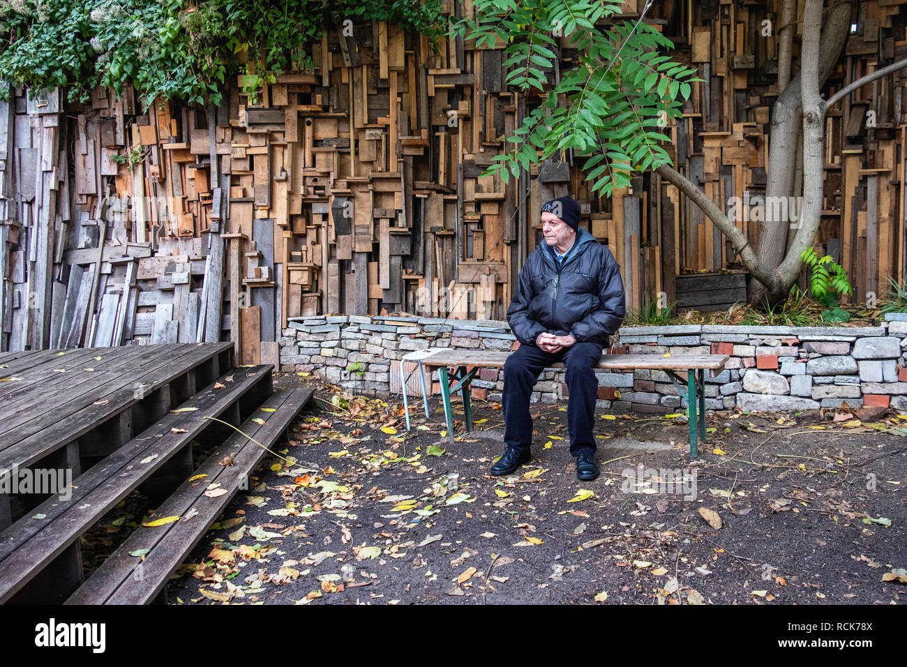 Berlin, Kreuzberg.Princess Garden,jardin commun Prinzessinnengarten,lieu de rencontre communautaire.Senior homme assis en face de mur fait de bois recyclé Banque D'Images