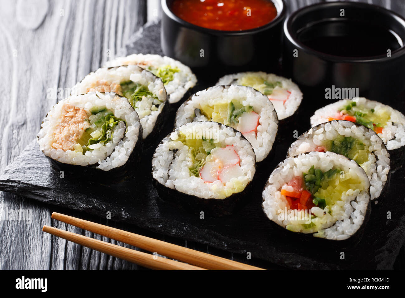 Rouleaux Futomaki avec divers matériaux ont servi avec des sauces close-up sur une liste de sélection sur la table horizontale. Banque D'Images